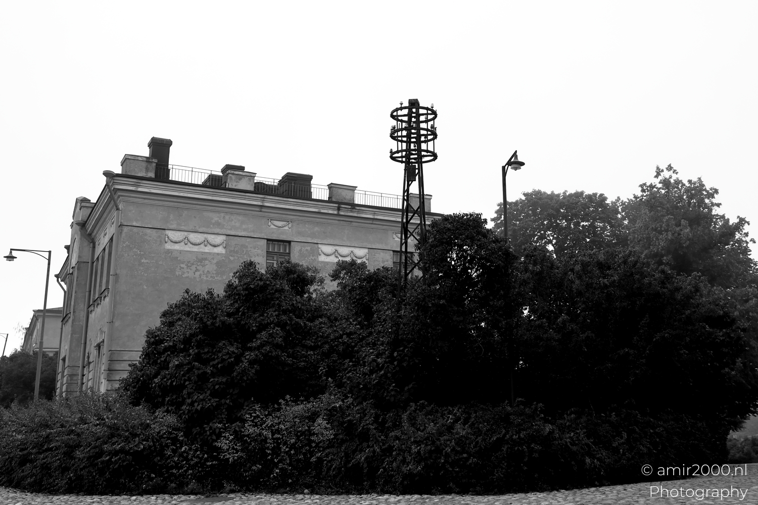 Black and white view of old Suomenlinna building with tower and dense bushes under a bright misty sky