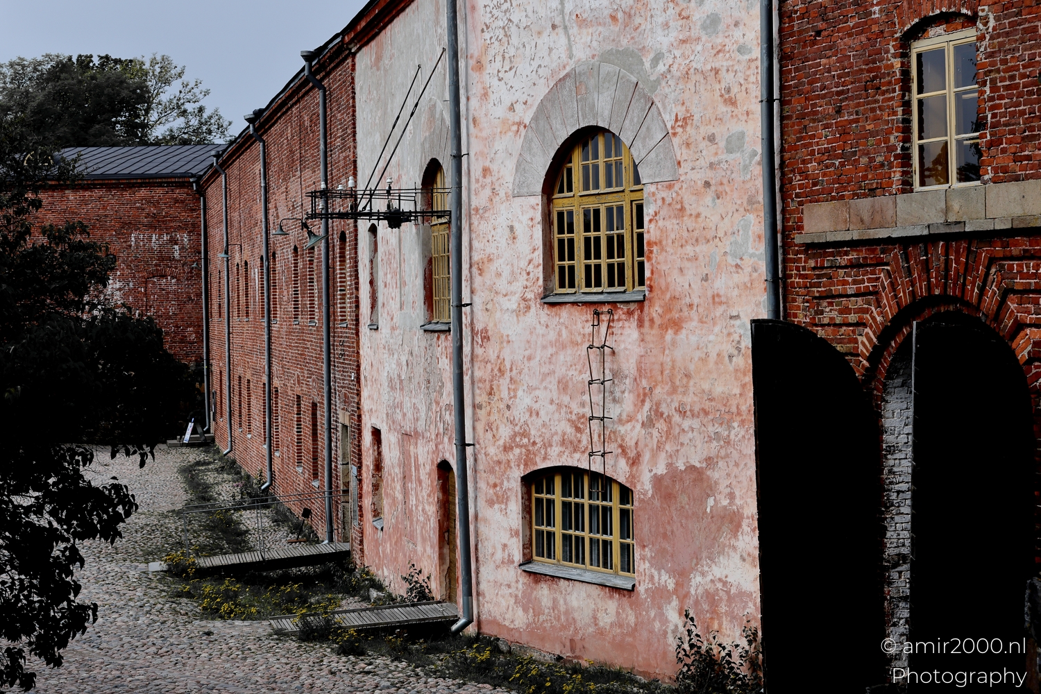Row of old brick and plaster buildings at Suomenlinna with cobblestone courtyard and muted morning colours