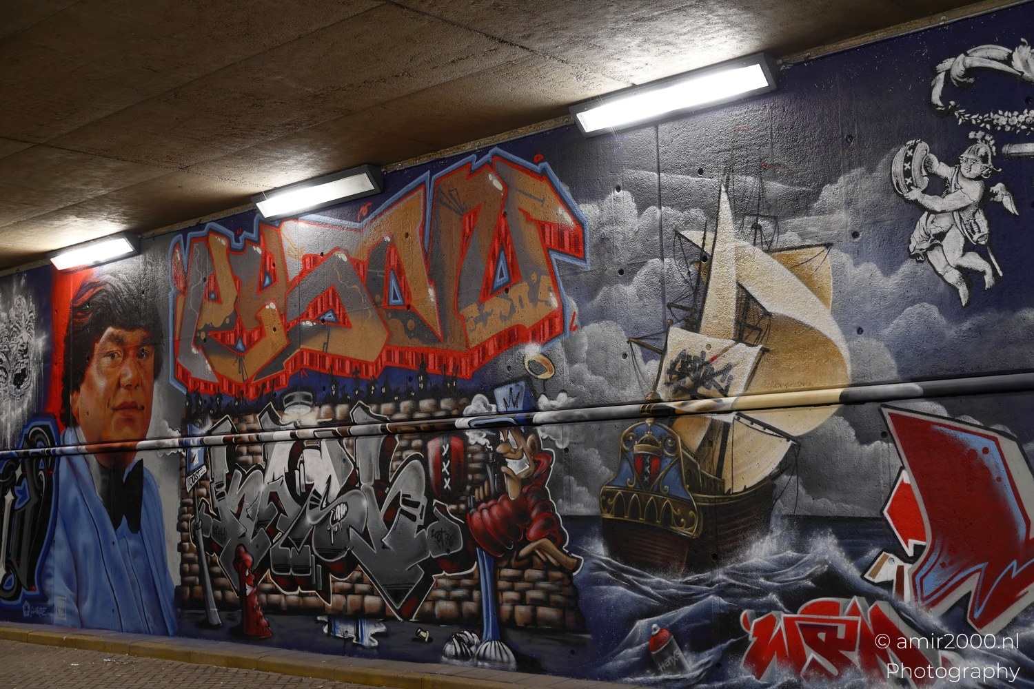 Wide view of tunnel wall with film character portrait, golden graffiti lettering and sailing ship in artificial light