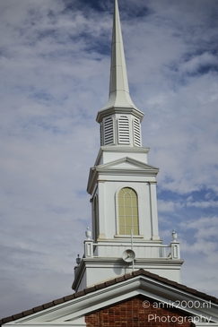 A white church building with a prominent spire and arched window against a blue sky. - image from year 2025 #001