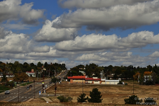 A suburban street with commercial and residential buildings under partly cloudy skies. - image from year 2025 #001
