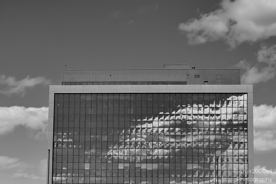 A modern building with reflective windows mirrors a cloudy sky. - image from year 2025 #005