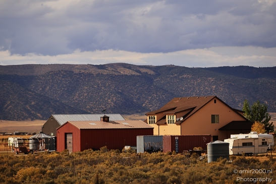 A rural farm with a red barn and an orange house in front of mountainous terrain. - image from year 2025 #002