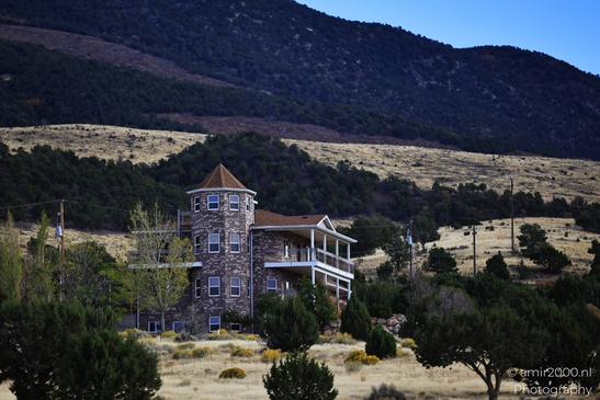 A multi-story building with a turret and balcony overlooks an arid landscape near mountains. - image from year 2025 #003
