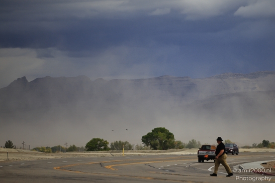 A man walks across a parking lot with dramatic mountainous backdrop under cloudy skies. - image from year 2025 #005