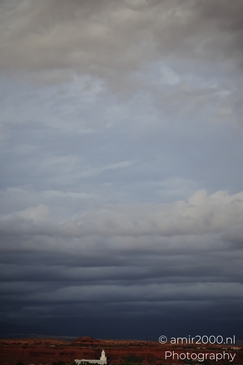 Storm clouds gather over a rural landscape with reddish terrain and sparse vegetation. - image from year 2025 #002