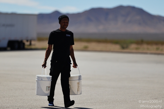 Man Carrying Buckets in Arizona USA. A man in a black shirt carries two white buckets across a - image from year 2025 #001