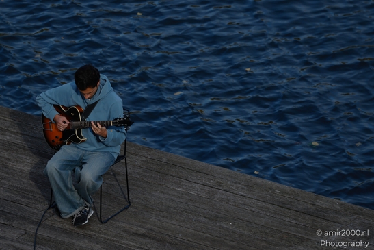 Man_Playing_Guitar_On_Wooden_Dock_At_Dusk_On_Canal_Edge_Amsterdam_Netherlands_People_Creative_Collection_Photography_Canon_EOS_R5_Mark_II_2025_001.JPG