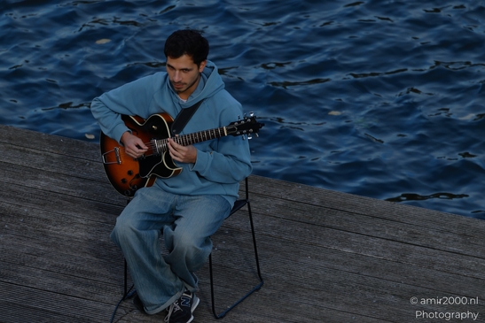 Man_Playing_Guitar_On_Wooden_Dock_At_Dusk_On_Canal_Edge_Amsterdam_Netherlands_People_Creative_Collection_Photography_Canon_EOS_R5_Mark_II_2025_002.JPG