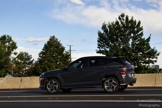 A dark-colored SUV driving on an urban highway with foliage and clear skies in the background. - image from year 2025 #016
