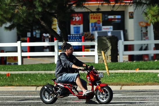 A man riding a red mini motorcycle on the road near a gas station. - image from year 2025 #001