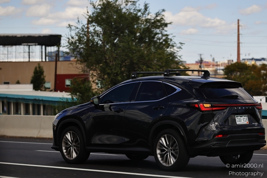A black Lexus SUV is driving on a highway with an urban backdrop. - image from year 2025 #004