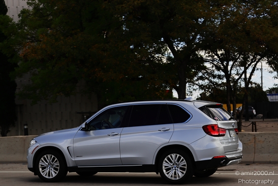 A silver BMW SUV is driving on a highway with greenery and buildings in the background. - image from year 2025 #006