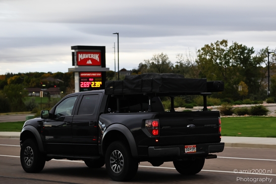 A dark-colored pickup truck is driving on a highway with cargo covered by a black camouflaged - image from year 2025 #001