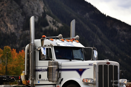 A white semi-truck parked on a mountain road with autumn foliage in the background. - image from year 2025 #001