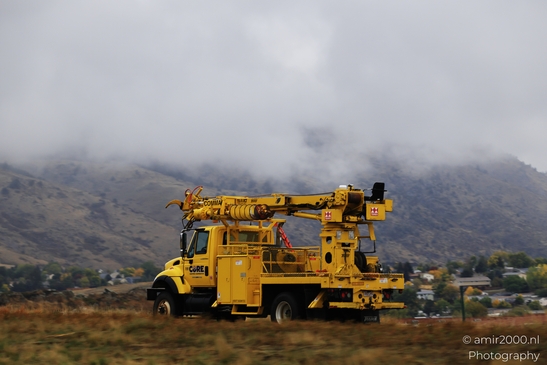 A yellow utility truck parked on a roadside near mountains with foggy clouds in Colorado. - image from year 2025 #001