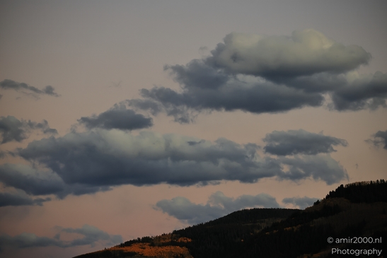 Dark clouds hovering above mountains during sunset with orange tree hues. image from year 2025 #1