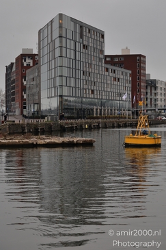 A modern glass-fronted building reflected in water with a yellow buoy nearby. - image from year 2025 #001