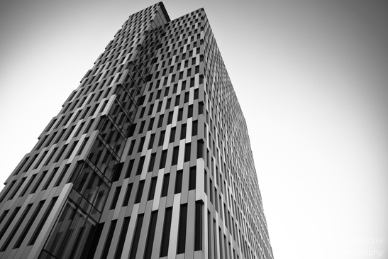 A tall skyscraper with a geometric facade stands against the clear sky. - image from year 2025 #007