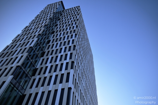 A towering skyscraper with a reflective glass facade stands prominently in the Amsterdam - image from year 2025 #008