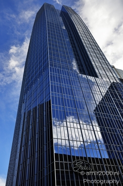 A modern skyscraper with a reflective glass facade under a partly cloudy sky. - image from year 2025 #002
