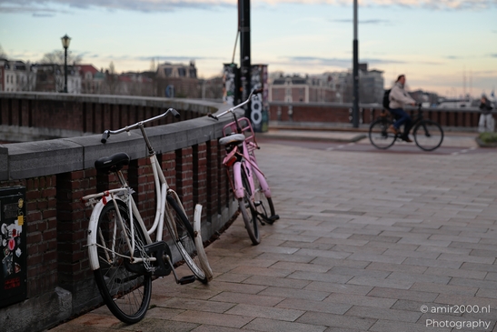Bicycles_On_Urban_Bridge_At_Sunrise_With_Cyclist_Passing_Amsterdam_Netherlands_Cityscape_Photography_Canon_EOS_R5_Mark_II_2025_001.JPG