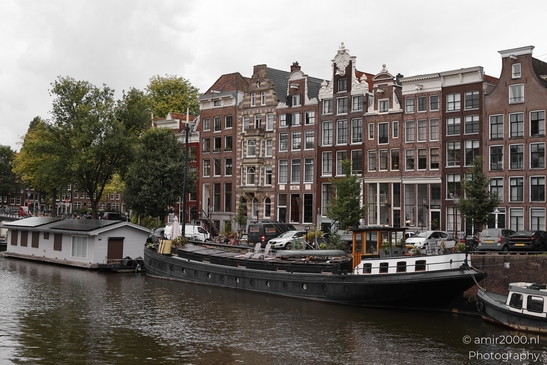 A picturesque view of Amsterdam's city center with traditional Dutch canal houses and boats on a - image from year 2025 #002