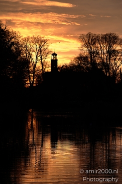 A serene sunrise scene with silhouetted trees and a church steeple reflected in still water near - image from year 2025 #001