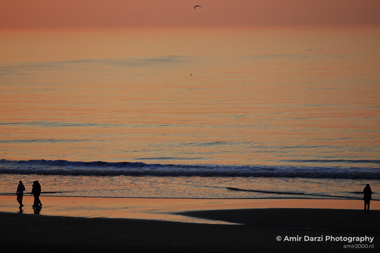 A beach scene at dusk, with two people walking on the sand and the ocean stretching into the distance.