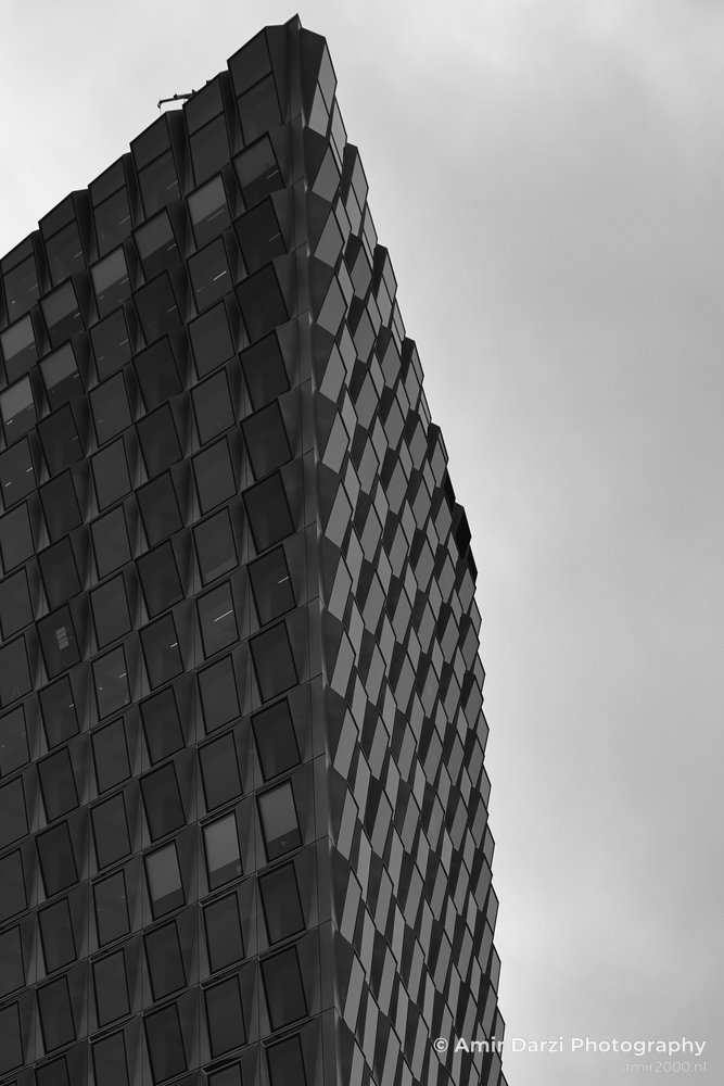 Black and white photograph of an angular building with reflective windows under cloudy skies.