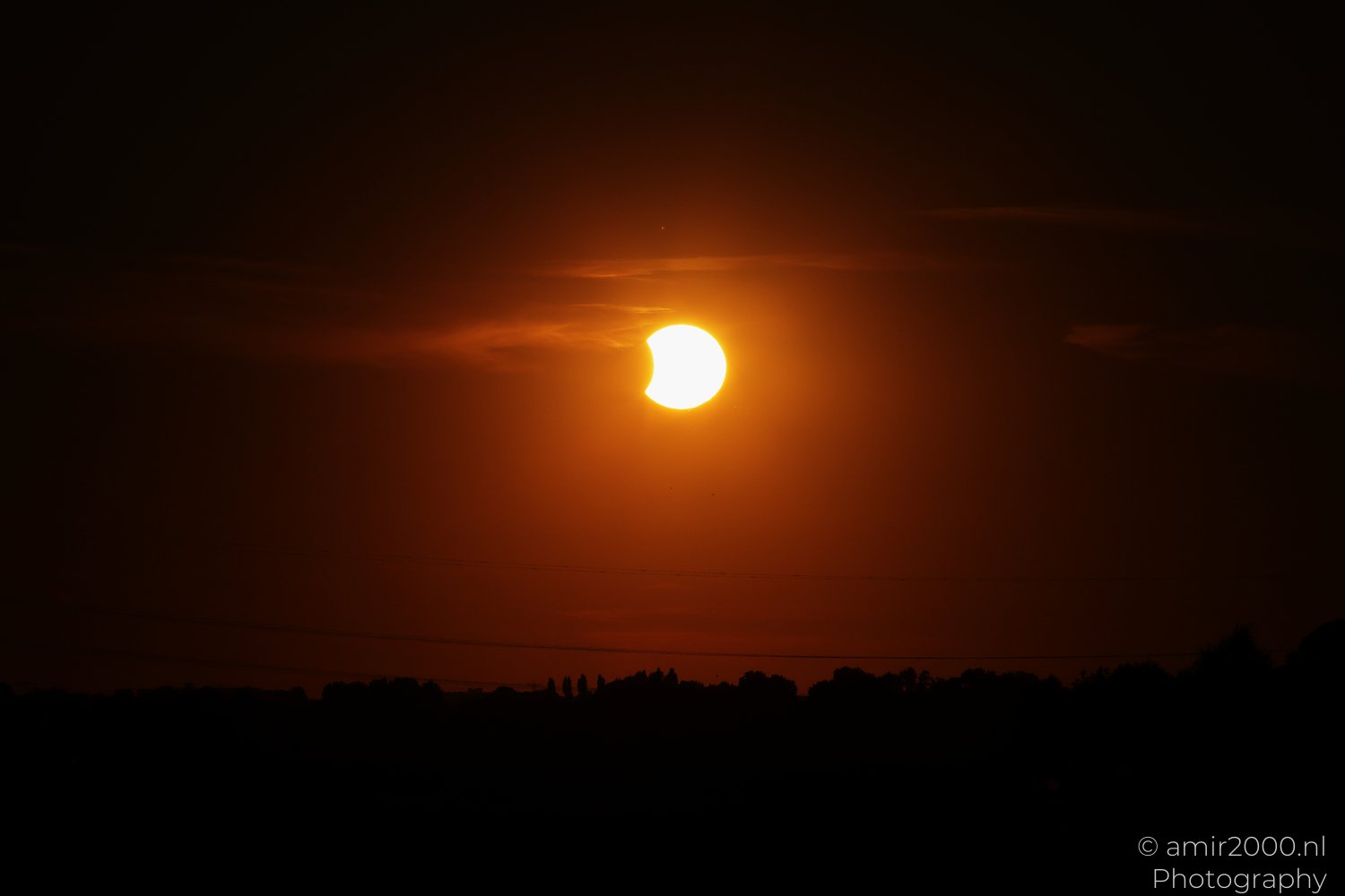 Partially eclipsed Sun descending over Amsterdam in an orange evening sky