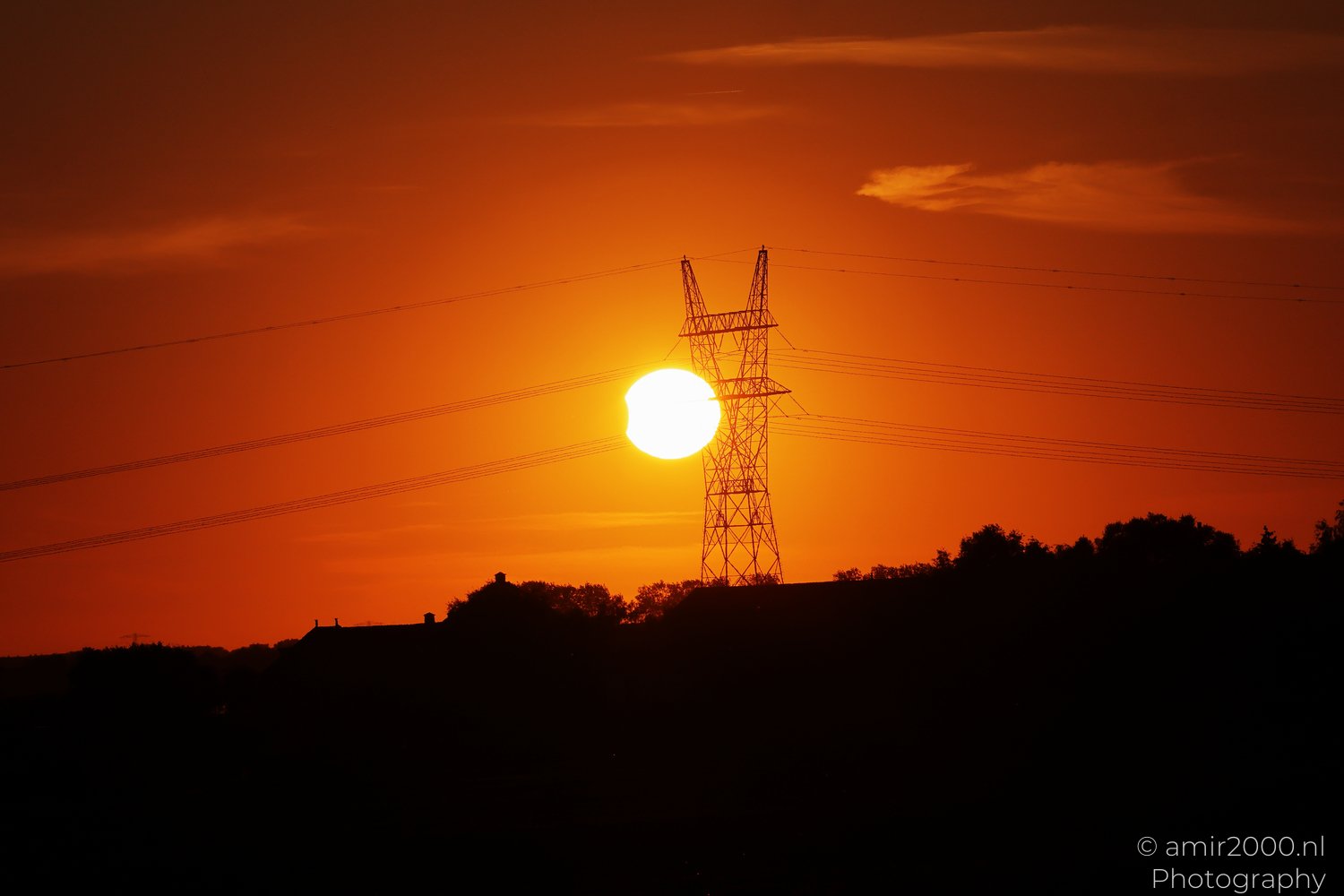 Partially eclipsed Sun setting beside an electricity pylon in Amsterdam