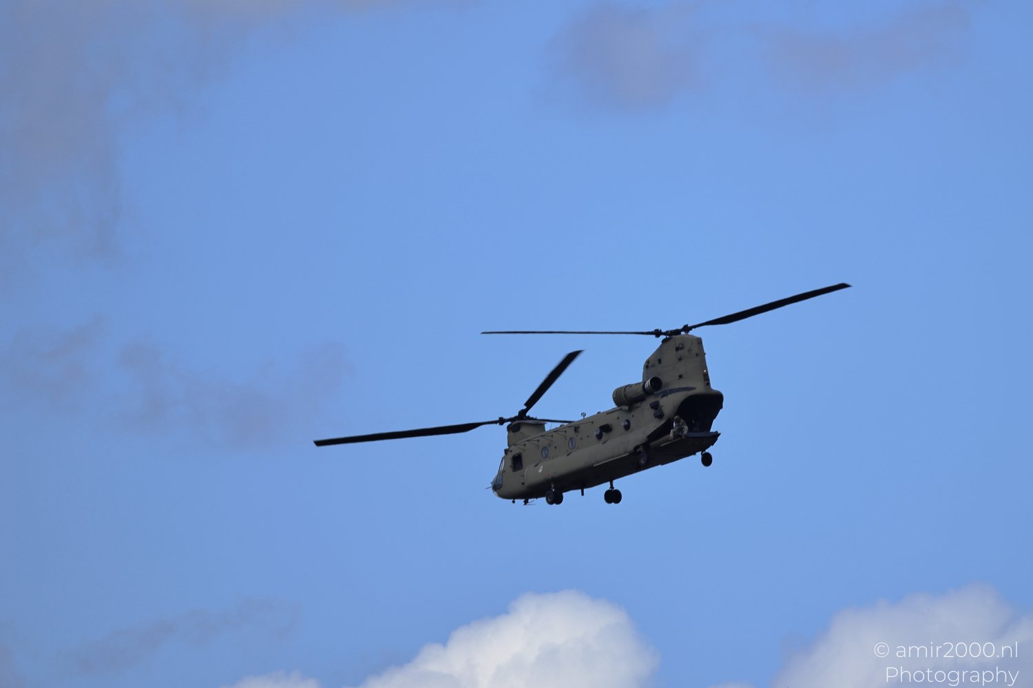 A military helicopter in flight against a blue sky with some clouds in Amsterdam, Netherlands.