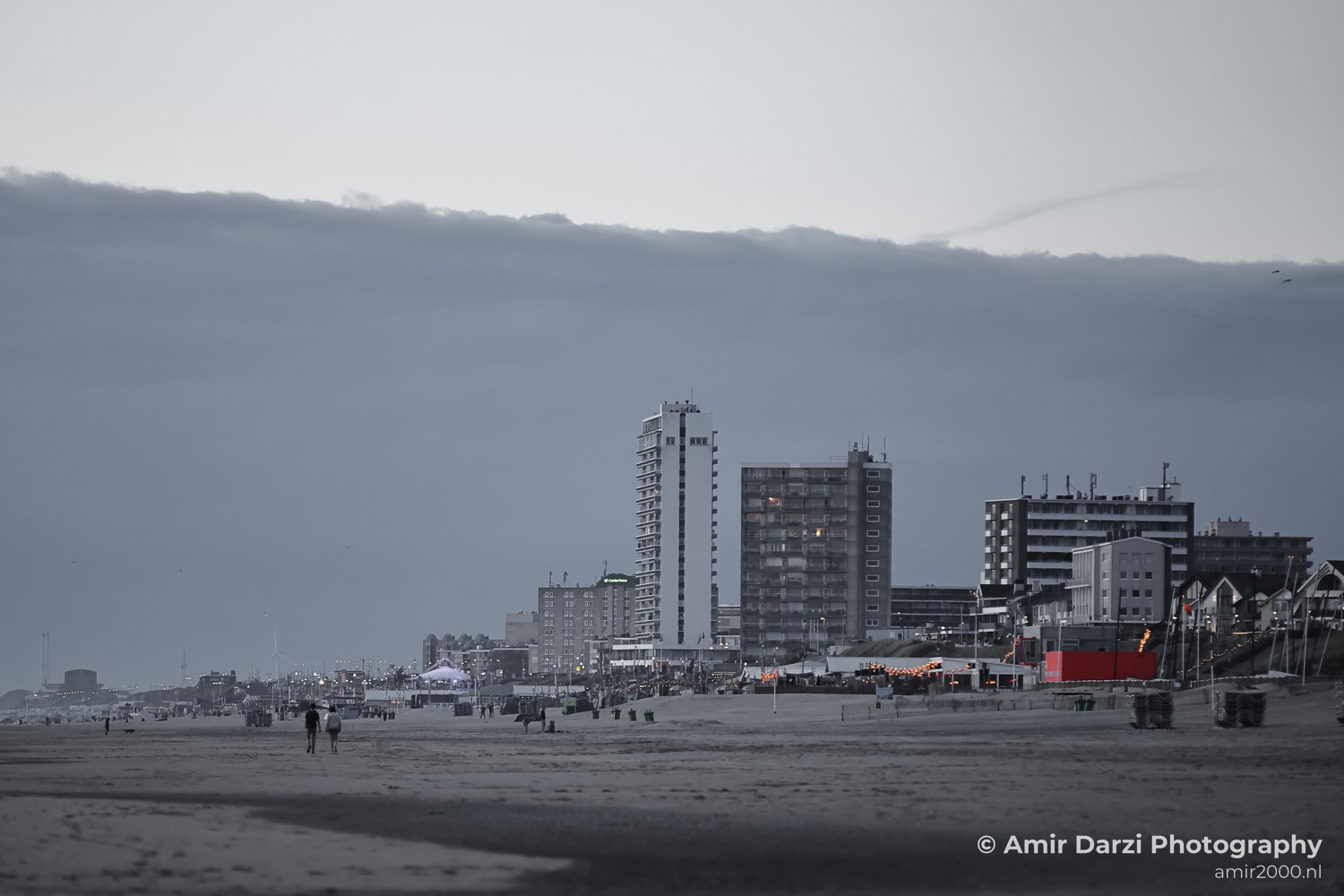 Evening beach scene with tall buildings and a darkening sky.