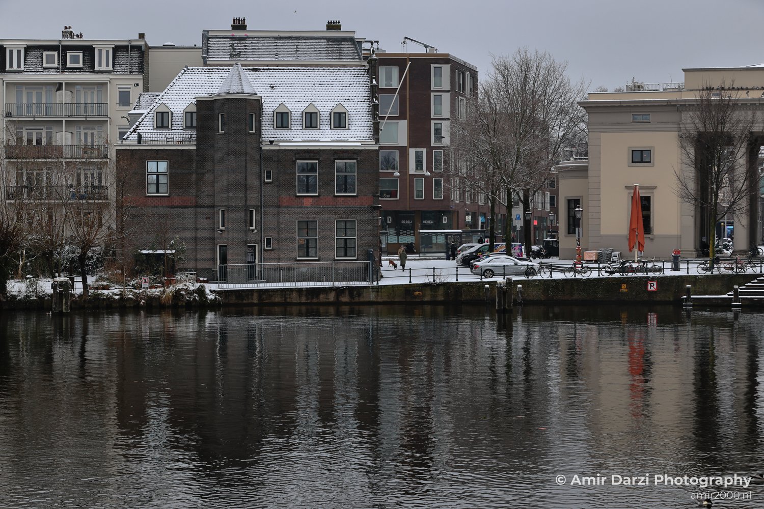 Snowy winter day featuring buildings and bicycles near a canal.