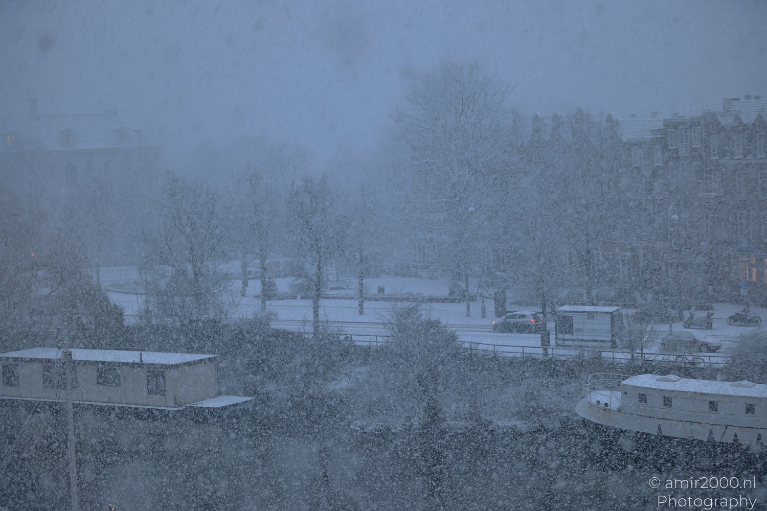 Heavy snowfall on residential and commercial buildings during dusk in the cityscape of Amsterdam.