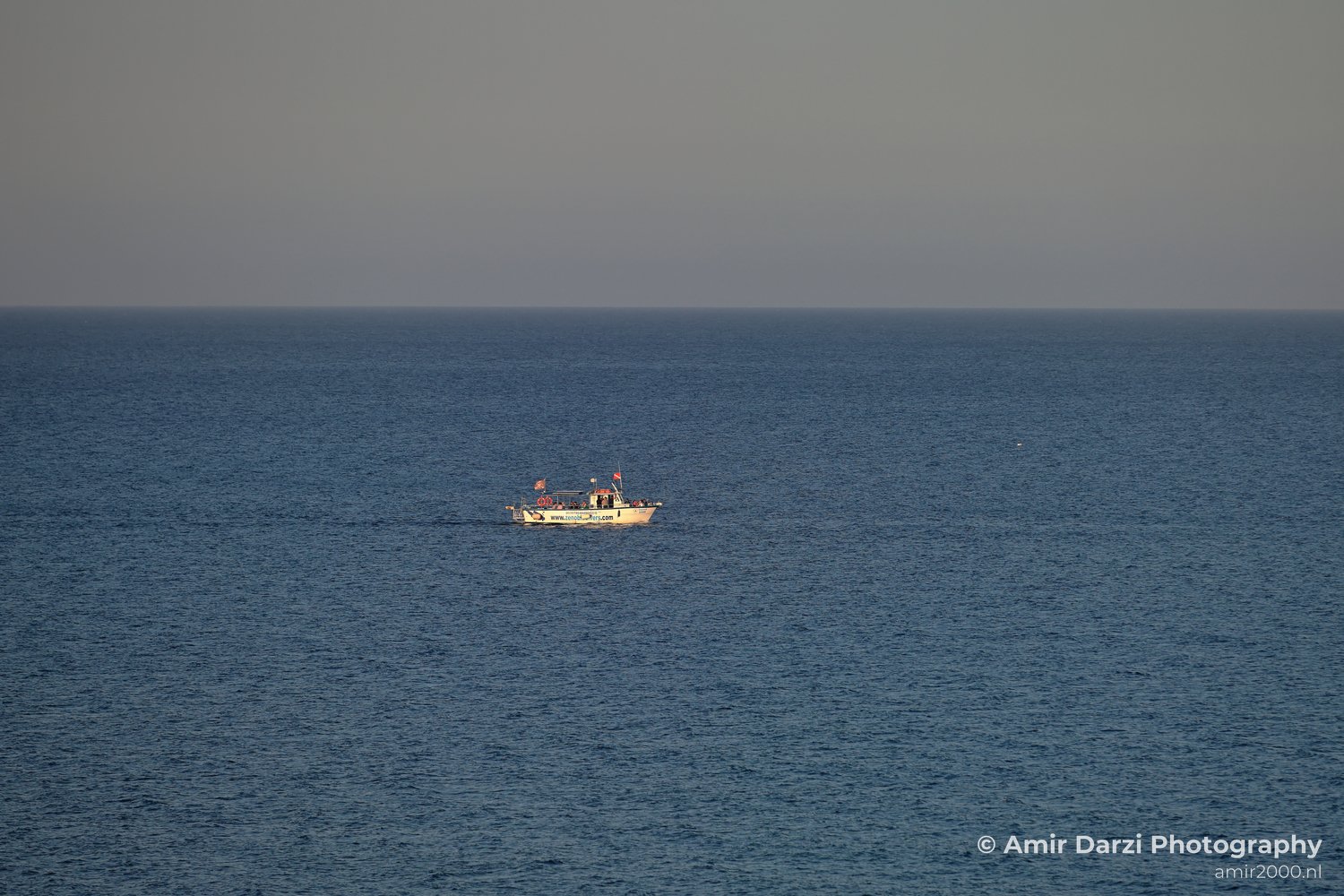 A clear sky appears above a small boat is centered in the middle of an expansive body of water in Larnaca, Cyprus.
