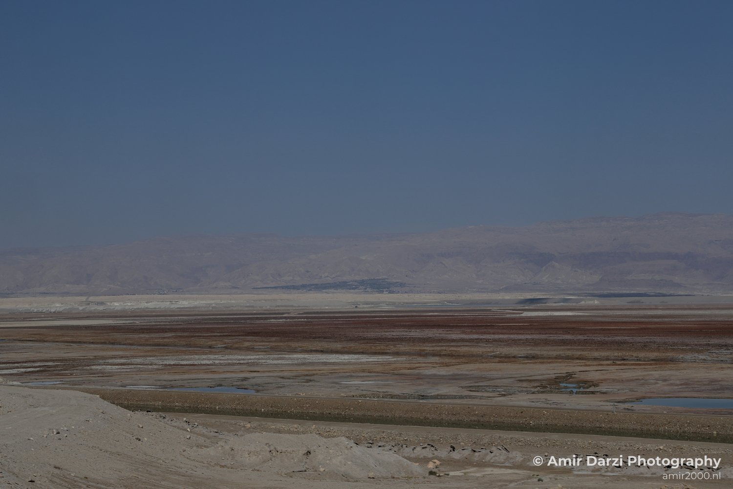 Sparse vegetation and small water bodies scattered across the terrain appears with the vast desert landscape in Dead Sea, Israel.