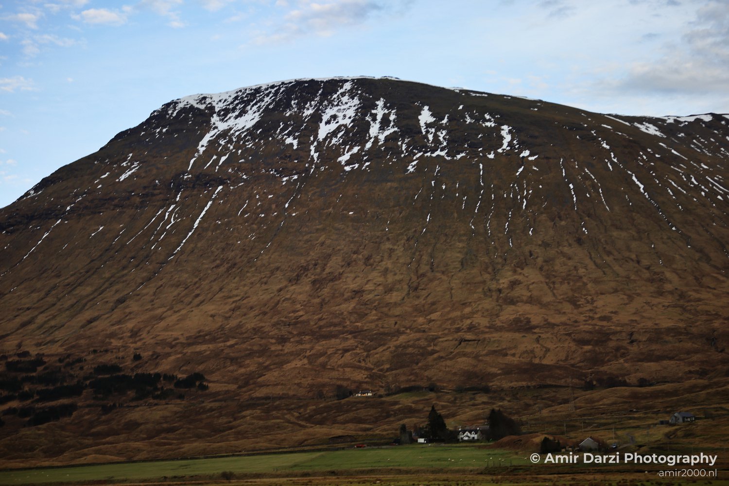 A scenic view of a snow capped mountain in Scotland with a quaint village.