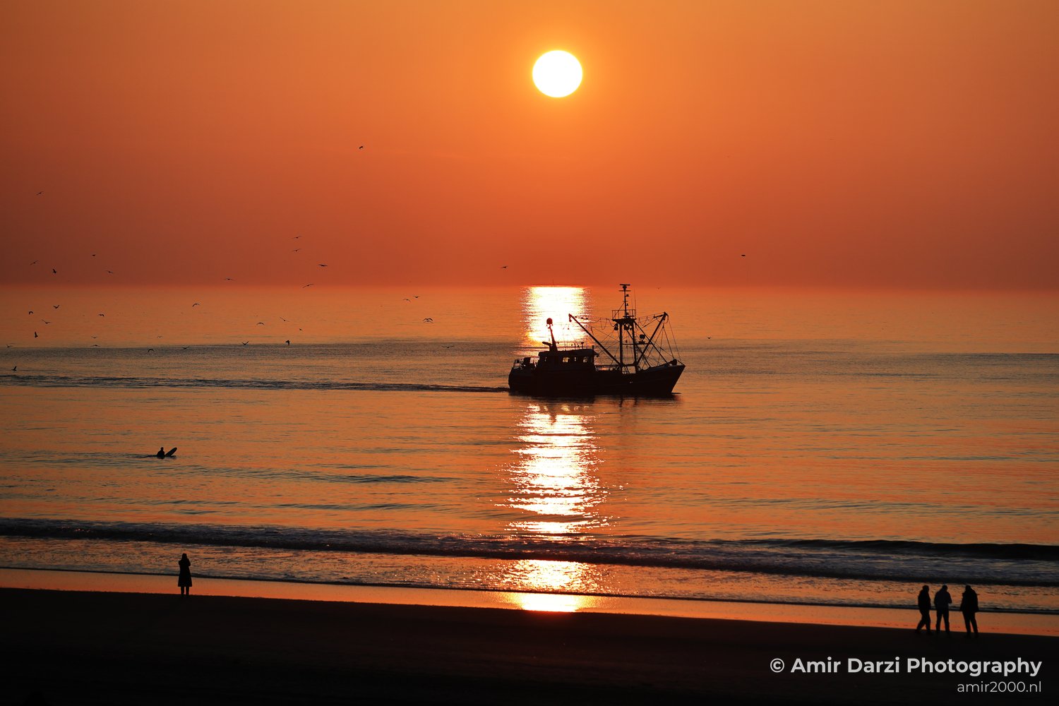 A scene at sunset with a fishing boat and a person on the beach, silhouetted against the orange sky.