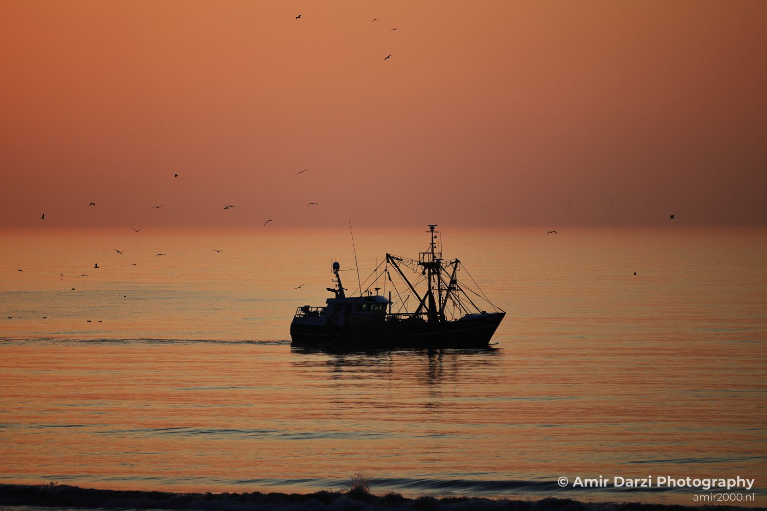 A fishing boat is anchored in the North Sea at sunset, with birds flying overhead and the horizon clearly.