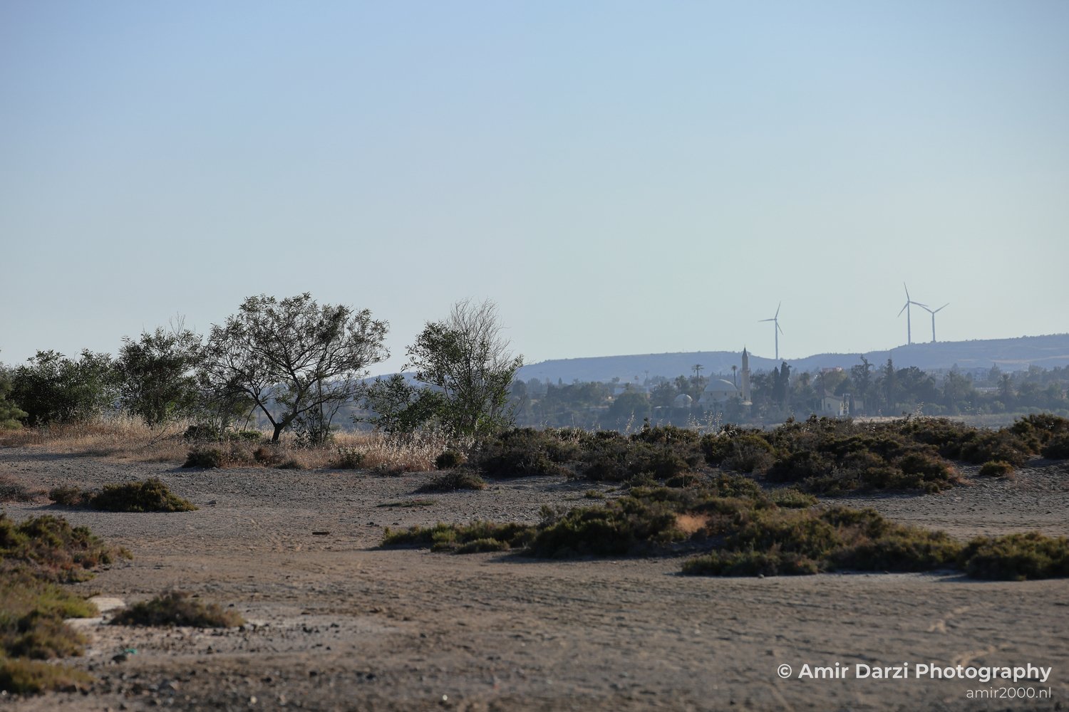 A desolate area with minimal greenery and two prominent windmills in the distance.