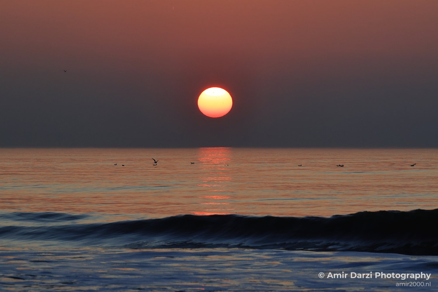 A sunset over the North Sea, with the sun setting behind the horizon and the water reflecting the colors of the sky.