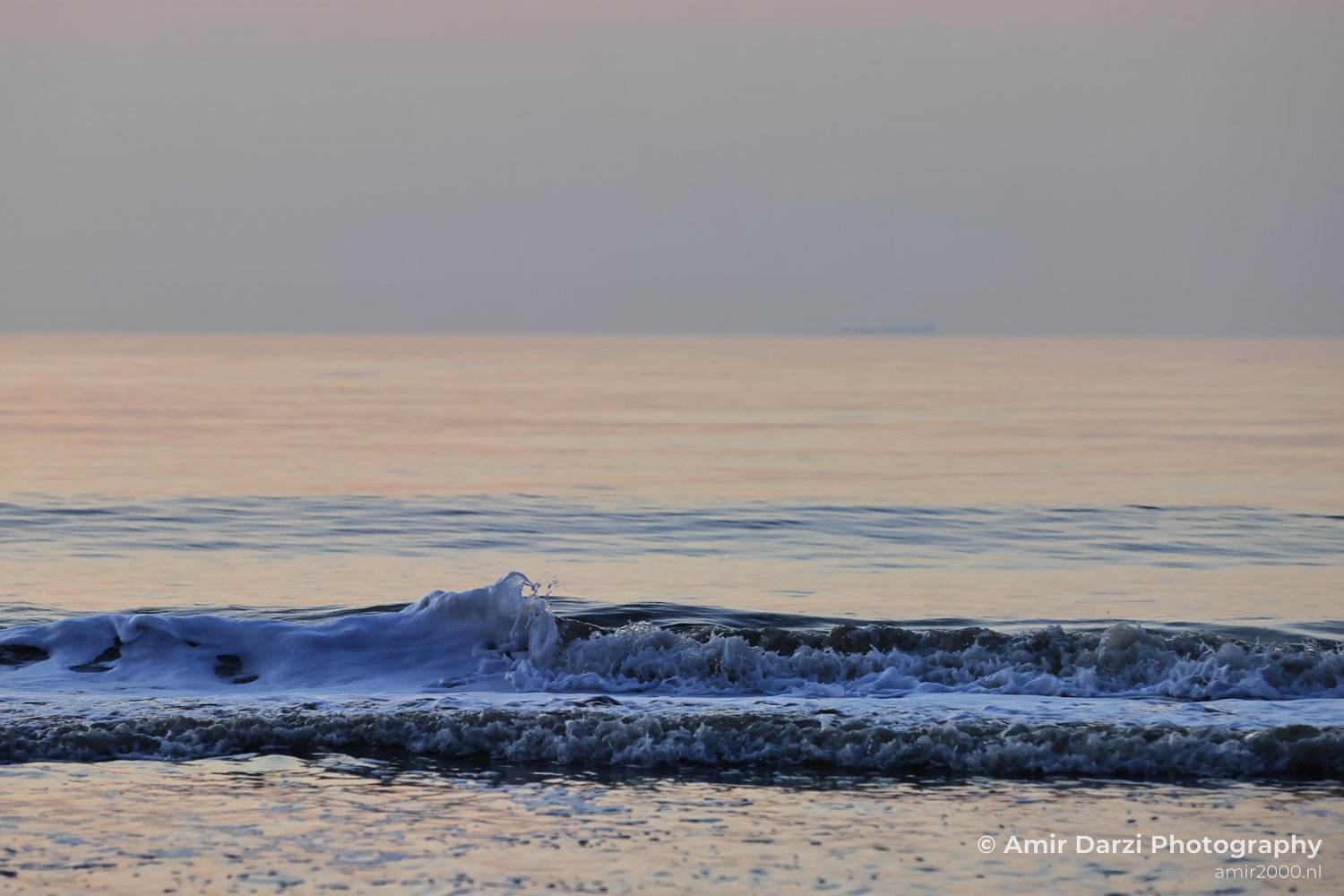 A sunset over the North Sea, with waves gently crashing onto the beach.