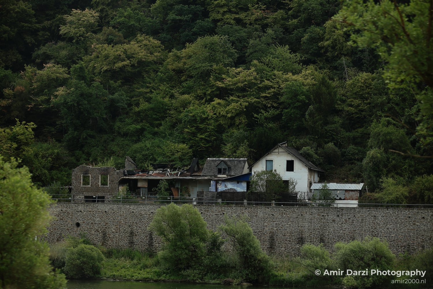 A cluster of buildings and a dense forest in the background appears alongside a stone wall in the foreground in Rhineland Palatinate, Germany.