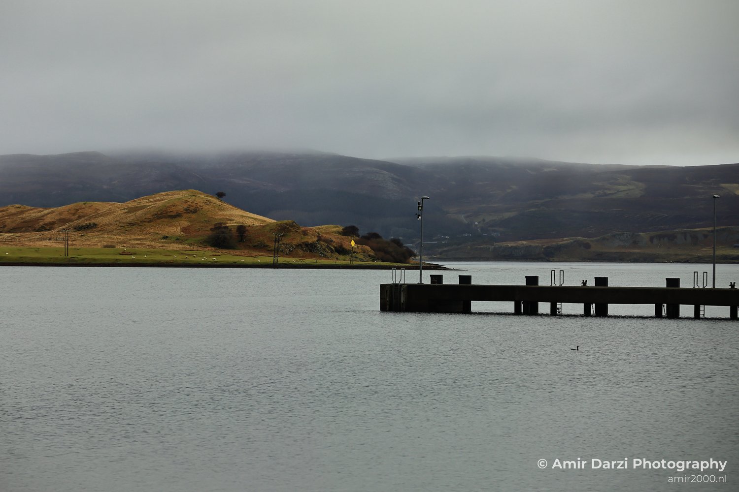 A concrete pier extending into it on the right side appears with the calm body of water in Scotland United Kingdom.