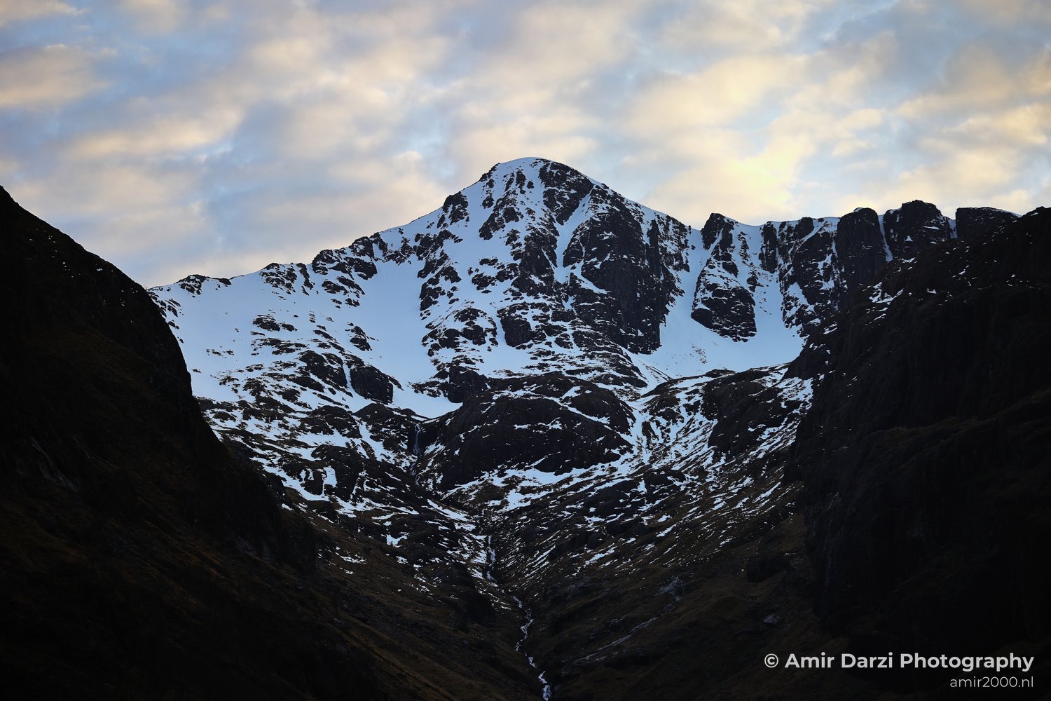 Snow covered peaks and rugged terrain under a partly cloudy sky add detail to the mountainous landscape in Scotland United Kingdom.