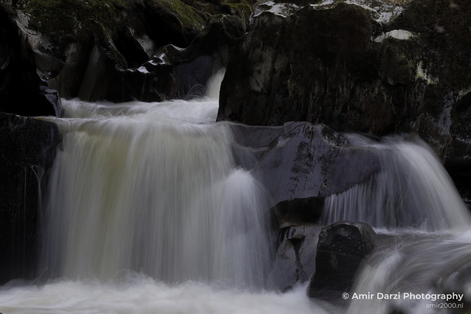 Moss and patches of snow, creating a dynamic flow of water, appear with the waterfall cascading over dark rocks in Scotland United Kingdom.