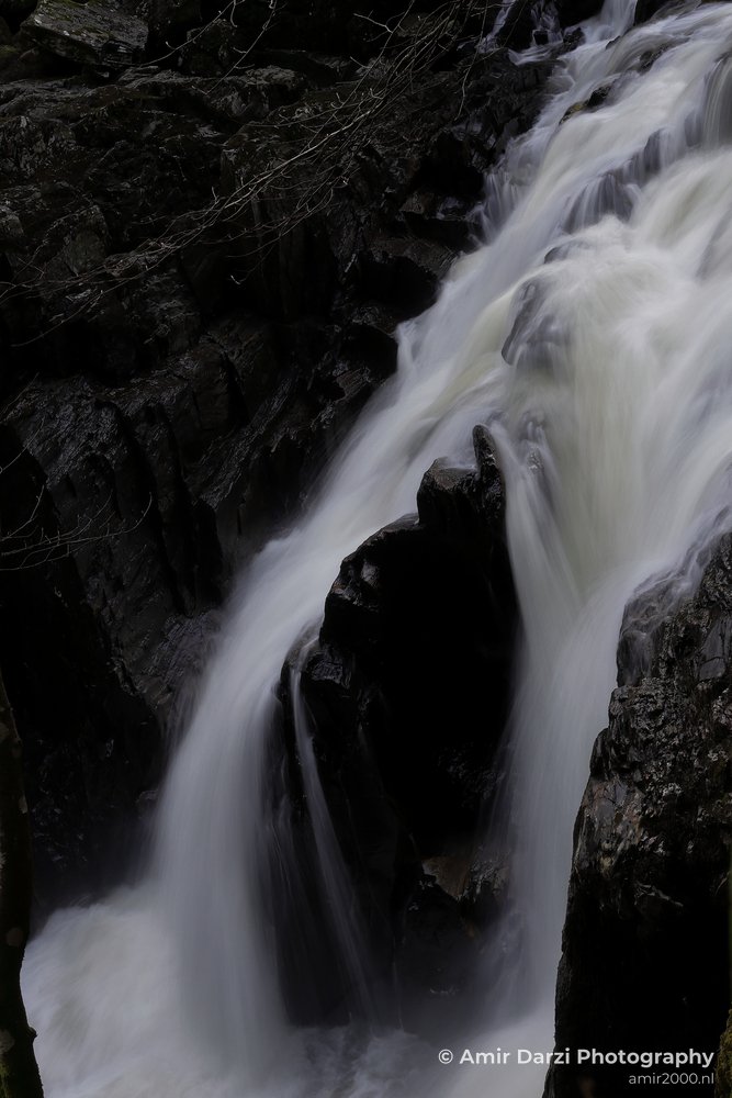 Some branches and twigs visible on top of the rocky terrain appear with the waterfall cascading down over dark rocks in Scotland United Kingdom.
