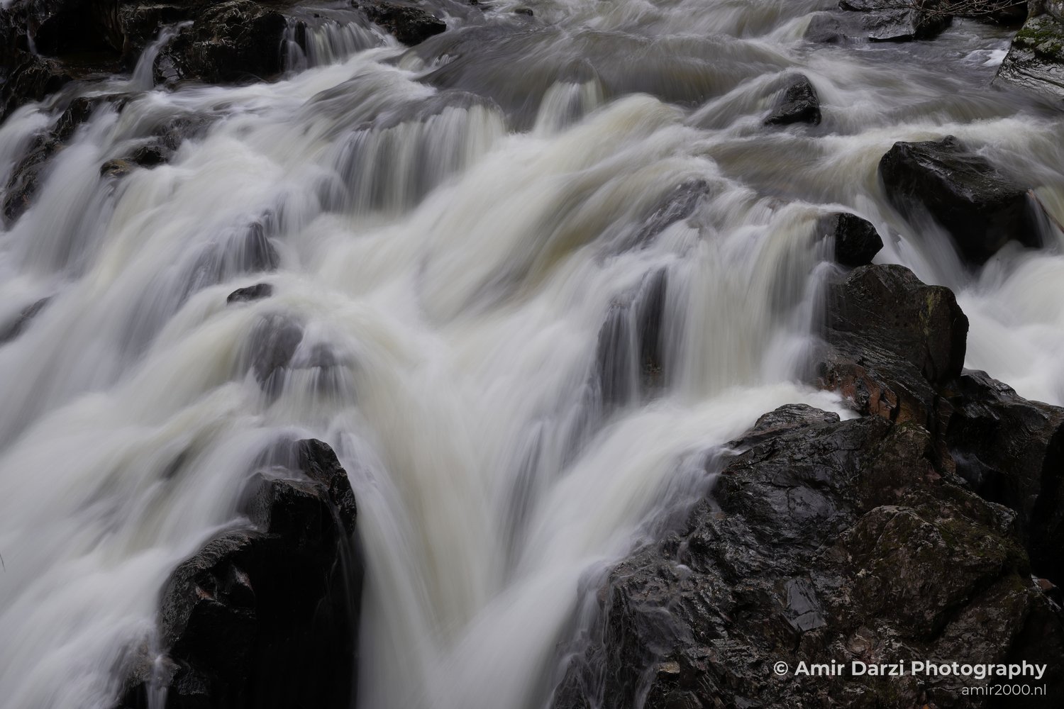 White water flowing vigorously and creating a blurred effect due to motion appears with the dynamic waterfall cascading over dark rocks in Scotland United Kingdom.
